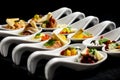 Two rows of canapes on white ceramic spoons. Black background