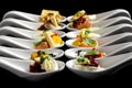 Two rows of canapes on white ceramic spoons. Black background