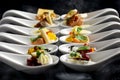 Two rows of canapes on white ceramic spoons. Black background with smoke