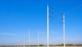 Two rows of electric poles with cable lines on curve country road against blue sky background, low angle and perspective side view Royalty Free Stock Photo