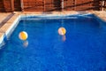 Two rubber air yellow white inflatable balls and toy for swimming pool in transparent blue water. Beach balls floating on water. Royalty Free Stock Photo