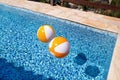 Two rubber air yellow white inflatable balls and toy for swimming pool in transparent blue water. Beach balls floating on water. Royalty Free Stock Photo