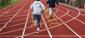 Two runners running over six iinch hurdles in lane on a track