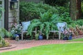 Two rustic chairs with decorative pillows outside home with giant fern and potted plants surrounding in garden or yard