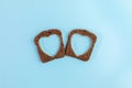 Two rye bread slices with carved holes of heart shape in them on light blue background. Creative minimal concept.