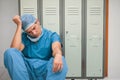 Hispanic male surgeon leaning against lockers in locker room, wearing scrubs and bouffant cap Royalty Free Stock Photo