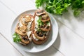 Two sandwiches with mushroom slices and curd cheese and fresh bright parsley lie on a white plate on a white background