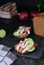 Two sandwiches with salted lard strips with meat strips and fresh cucumber on rye bread on a slate board on a black concrete