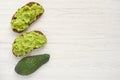 Two sandwiches or toast with avocado on grain bread and half raw avocado fruit on white wooden background. Top view, copy space