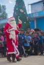 two Santa Clauses dancing in front of indigenous children with a tree in the background