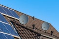 Two satellite dishes on the roof of a tiled house. Solar panels on the roof. Blue sky Royalty Free Stock Photo