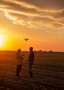 Two satisfied farmers standing in field using drone