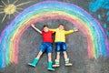 Two school kids boys having fun with with rainbow picture drawing with colorful chalks on asphalt. Siblings, twins and Royalty Free Stock Photo