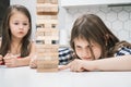 Two schoolgirls friends playing board game Jenga tower made of wooden blocks. Concentrated girl trying to pull detail.