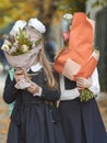 Two schoolgirls girlfriends are standing on the street hiding behind bouquets of flowers