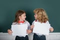 Two schoolkids holding white paper blank, poster with copy space. Schoolgirl and schoolboy in classroom at school Royalty Free Stock Photo