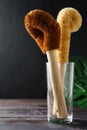 Two scrapers made of coconut bristles and a bamboo handle in a glass cup on a dark background. Royalty Free Stock Photo
