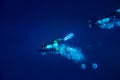 Two scuba divers swimming in deep blue seen from top making bubbles