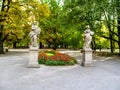 Two sculptures of ancient Roman goddesses on a background of yellow-orange-green trees and red flowers in the Saxon Garden in