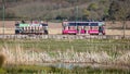 Two seaton tramway replica trams crossing in front of Seaton wetlands nature reserve in Seaton, Devon, UK