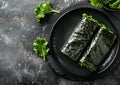 Two seaweed rolls on a black plate, resembling terrestrial plants on a table