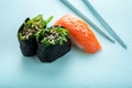 Two seaweed Sushi Chuka and sushi nigiri with salmon with chopsticks on a blue