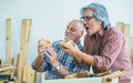 Two senior elderly retired happy men or carpenters wearing check shirt, creating wooden DIY furniture, cup for home decoration as