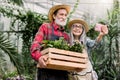 Two senior gardeners, man and woman in straw hats and checkered shirts, making photo together on smartphone posing with