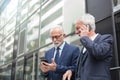 Two happy senior businessmen using smart phones, talking and messaging