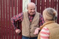 Two senior neighbors takling to each other on sunny day near fence.