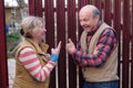 Two senior neighbors takling to each other on sunny day near fence