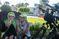 Two senior people cyclists with yellow helmet have a break in a green park eating a fruit and smiling. Moment of relaxation with Royalty Free Stock Photo