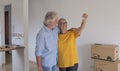 Two senior people hugging  holding the keys of the new empty apartment with moving boxes on the floor - concept of active elderly Royalty Free Stock Photo