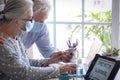 Two senior people man and woman with silver hair using laptop computer and  smartphone working from home wearing face mask due to Royalty Free Stock Photo