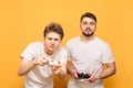 Two serious guys with joysticks in their hands play games on a yellow background. Two concentrated friends are playing video games Royalty Free Stock Photo