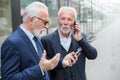 Two serious senior businessmen using mobile phones in front of an office building Royalty Free Stock Photo