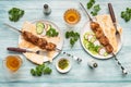 Two servings of appetizing homemade shish kebab, sliced cucumbers and radishes, glasses of wine on a blue wooden background.