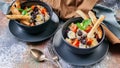 Two servings of Caesar salad with chicken, quail egg, cherry tomatoes, croutons and basil in dark blue bowls on a rusty background