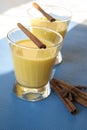 Two servings of golden milk in transparent glasses on a blue background, with spice