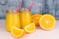 Two servings of orange juice in glass jars and fresh oranges on the table. Close-up.