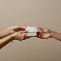 Two sets of hands exchanging a small white gift box tied with a ribbon Royalty Free Stock Photo