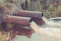 Two sewer pipes pour out to the river/Waste water flow from water pipe into lake. Toned Royalty Free Stock Photo
