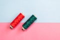Two sewing thread reels of red and green color on the pink and sky blue colored background. Used selective focus and copy space Royalty Free Stock Photo