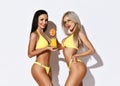 Two sexy slim beautiful girls in yellow bikini swimsuits squeeze fresh orange juice make cocktail smiling on white