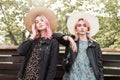 Two sexy young women with pink hair in trendy youth summer clothes from new collection in straw stylish hats stand near vintage Royalty Free Stock Photo