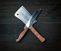 Two sharp knives lie on a brown wooden surface, kitchen items are crossed