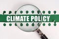 Between two sheets from a notebook on a green strip with the inscription - climate policy, there is a magnifying glass Royalty Free Stock Photo