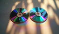 Two shiny cds rest on a textured surface. Colorful light refractions cast rainbow patterns from optical discs. Sunlight creates Royalty Free Stock Photo