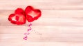 two shiny red heart-shaped balloons with pink and silver ribbons on a beige and pink wooden background. Valentine&#s Day