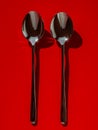 Two Shiny Stainless Steel Spoons on Vibrant Red Background Modern Kitchen Utensils Concept